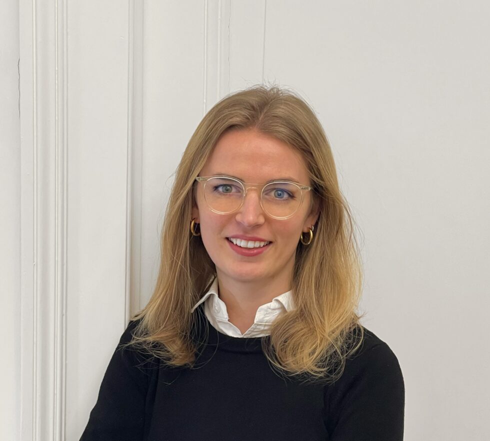 Das Portraitfoto einer Frau mit Brille und Pullover vor neutralem Hintergrund